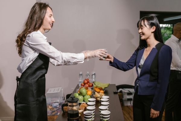 Two professionals interacting at a catered business event with coffee and fruit.