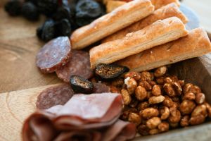 A beautifully arranged charcuterie board featuring salami, breadsticks, nuts, and dried fruit.